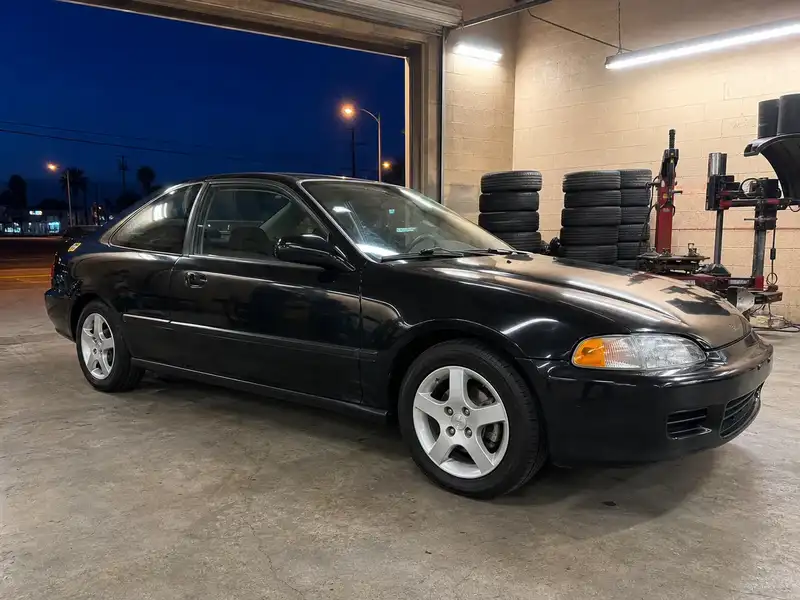 Black coupe with new tires under shop work lights